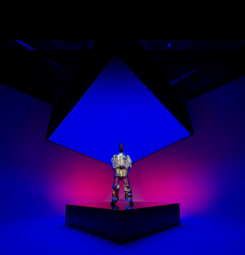 A person dressed in a metallic suit standing on a square centre stage and encompassing the background showcasing the Ultra Wide camera on iPhone 16 Pro Max